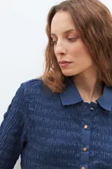 Camisa de manga corta en color bordó, confeccionada en tejido con textura de punto smock. Presenta cuello clásico, cierre frontal con botones y un ajuste entallado al cuerpo.