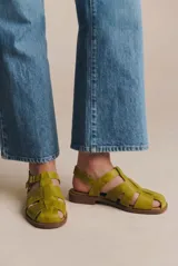 Sandalia tipo cangrejera de cuero lavado color mostaza, con diseño de tiras cruzadas, puntera cerrada y cierre con hebilla metálica en el tobillo. Cuenta con suela plana de goma.