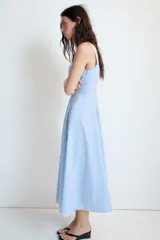 Vestido midi de color celeste con escote cuadrado y tirantes anchos. Presenta un diseño entallado en el torso con falda acampanada terminada en godets que aportan volumen y movimiento. Incluye cierre lateral con cremallera oculta.