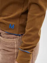 Polera de manga larga confeccionada en tela rib color bordó, con cuello alto y hombreras. Presenta costuras a la vista con pespuntes en hilo de color contrastante en el cuello, puños, hombros y ruedo.