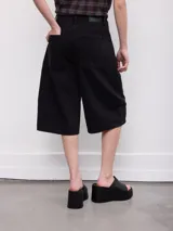 Bermuda de jean negra, de corte amplio y largo por debajo de la rodilla, con bolsillos traseros grandes y trabillas para cinto.