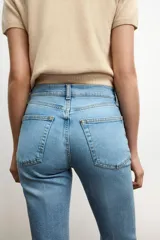 Jeans de mezclilla azul claro, tiro medio, corte recto y ligeramente acampanado en el bajo. Presenta cinco bolsillos y cierre frontal con cremallera y botón metálico.