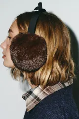 Orejeras tipo diadema con estructura de vincha negra y detalle de lazo en la parte superior. Presentan almohadillas con textura de pelo sintético en color marrón.