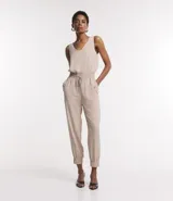 Mono largo de tejido plano color beige claro, sin mangas, con escote en V y elástico fruncido en la cintura. El pantalón es de corte jogger con puños ajustados.