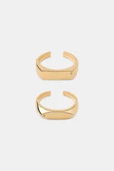 Pack de dos pulseras abiertas (tipo brazalete) de metal color dorado, con diseño rectangular y una pequeña aplicación de cristal o joya en un extremo.