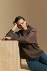 Polera de tejido acanalado en color marrón con detalles de líneas en tono lila, cuello alto y mangas largas con diseño raglán.
