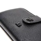 Billetera rectangular de cuero sintético con textura granulada, color negro. Cuenta con cierre superior, solapa frontal con broche a presión decorado con una flor metálica y logo de la marca grabado en el centro.