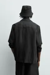 Camisa negra de manga corta, confeccionada en lino con corte relaxed fit, cuello bowling y cierre frontal de botonadura.