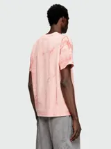 Remera de manga corta, cuello redondo y calce holgado, color rosa pálido con un efecto de teñido o estampado que simula grietas o craquelado en tonos más oscuros de rosa/naranja.