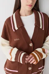 Cardigan de punto color chocolate con diseño de bloques de color y detalles a rayas en cuello, puños y ruedo. Presenta cierre frontal con botones, cuello tipo polo y dos bolsillos delanteros.