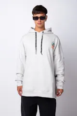 Buzo canguro oversize de algodón rústico, color gris claro, con capucha y cordones ajustables con logo estampado. Presenta un diseño gráfico pequeño en el pecho y detalles estampados en la manga.