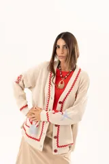Saco tipo cardigan oversize de punto color beige, con diseño temático marino que incluye bordados de corales, peces, estrellas de mar y tortugas. Presenta detalles de galón picot en color rojo en los bordes y puños, cierre frontal con botones al tono y corte holgado.