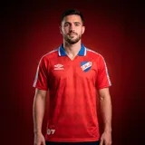Camiseta de fútbol Umbro del Club Nacional de Football, edición especial retro en colaboración con EA Sports. Diseño en color rojo con patrón geométrico sutil, cuello polo azul con detalles en blanco y rojo, y bandas laterales en las mangas con el logo de Umbro. Incluye escudo del club y logo de la marca.
