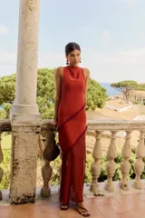 Vestido largo color caldera de silueta ajustada, con escote bote sin mangas y detalle de franjas diagonales con flecos. Presenta falda larga con sección inferior transparente.
