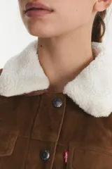 Campera tipo trucker de gamuza sintética color marrón, con cuello de corderito blanco, cierre frontal con botones metálicos y bolsillos en el pecho.