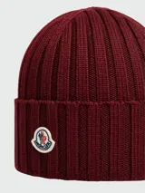 Gorro de lana tejido a punto acanalado, color bordó, con parche circular del logo de Moncler en el frente.