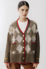 Saco tipo cardigan de punto con diseño de rombos en tonos marrón chocolate y beige. Presenta cierre frontal con botones grandes, cuello en V con borde en color rojo, dos bolsillos delanteros con ribete rojo y detalles bordados pequeños. Posee mangas largas con una franja horizontal en color mostaza cerca del puño.