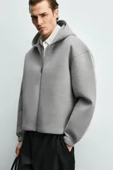 Sudadera gris de corte boxy fit con capucha y cierre frontal de cremallera. Confeccionada en tejido doble y compacto, cuenta con bolsillos laterales ocultos en la cadera y mangas largas con puños elásticos.