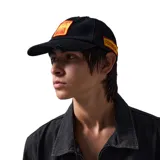 Gorra de béisbol negra con visera curva y parche bordado en el frente con diseño abstracto en amarillo y rojo. Presenta detalles desgastados y roturas en la visera y el frente.