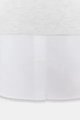 Camisa blanca de manga larga con un top de sudadera gris claro superpuesto, que incluye capucha ajustable con cordones. El bajo de la camisa tiene aberturas laterales.