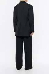 Chaqueta negra estilo sastre cruzada, de corte ajustado en cintura, con escote con solapas, manga larga y cierre frontal con botonadura. Incluye bolsillos con tapeta y abertura en la parte posterior.