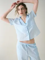 Camisa de manga corta para dormir confeccionada en broderie de algodón, con cuello solapa y cierre frontal con botones. Presenta un bolsillo aplicado en el pecho.