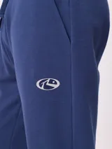 Babucha jogger color gris oscuro, con cintura elástica ajustable con cordón, bolsillos laterales y puños elásticos en los tobillos. Presenta un logo estampado en el muslo izquierdo.