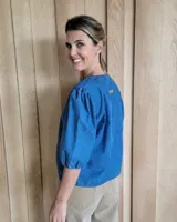 Blusa celeste de mangas 3/4 abullonadas, escote en V con detalle de bordado y lazo decorativo.