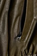 Cazadora estilo bomber color marrón oscuro, con efecto piel, cuello subido y manga larga. Tiene bolsillos delanteros con cierre de cremallera y acabados elásticos en puños y bajo. El cierre frontal es con cremallera y botones a presión ocultos.