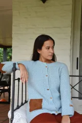 Saco de lana merino tejido a mano con dos agujas, color celeste, con botones de madera y apliques de cuero marrón en los bolsillos y codos.