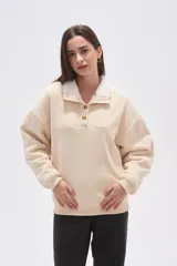 Buzo de algodón color beige con cuello tipo polo forrado en corderito blanco y cierre frontal con botones. Presenta mangas largas con puños elásticos y corte holgado.