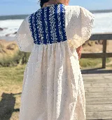 Túnica de lino color crudo con corte holgado y mangas cortas. Presenta una pechera cuadrada en el frente y la espalda confeccionada con textiles antiguos en color azul con patrones geométricos de ondas.