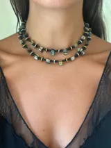 Gargantilla doble de estilo artesanal, compuesta por cuentas de nácar teñido intercaladas con discos metálicos en tonos dorado y plateado, y mostacillas negras. El diseño presenta una estructura de dos niveles que rodea el cuello.