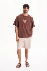 Remera oversize de manga corta en color marrón, confeccionada en 100% algodón. Presenta un diseño gráfico estampado en la espalda con inscripciones en color blanco.