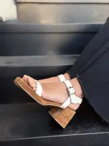 Sandalias de cuero color crudo, con dos tiras anchas sobre el empeine, pulsera al tobillo con hebilla y taco cuadrado de madera.