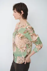 Camisa de manga larga con fondo verde y estampado floral en tonos rosados y beige, cuello redondo con pequeña abertura en V y cierre frontal con botones.