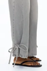Jean barrel de tiro alto confeccionado en denim de algodón rígido color gris claro con efecto deslavado, diseño curvo en las piernas y tiras finas para anudar en los bajos.