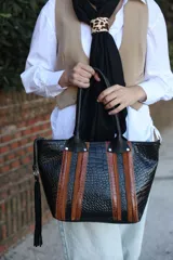 Cartera tipo shopper de cuero vacuno con textura crocco en color negro y detalles verticales en color whisky. Cuenta con doble asa de hombro y un colgante de borla lateral.
