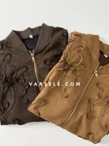 Campera tipo bomber confeccionada en gamuza, con cierre frontal metálico y detalle de flores bordadas en relieve en el frente.