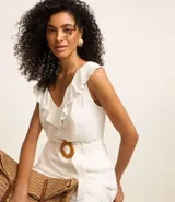 Enterito corto blanco sin mangas confeccionado en viscolino con escote V, espalda descotada con volados en el escote. Posee cinturón con hebilla redonda de ráfia y trabillas en la cintura.