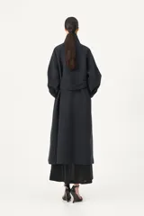 Tapado largo de corte amplio en color azul marino, confeccionado en una mezcla de poliéster y lana. Presenta un diseño con cuello camisero, cierre frontal mediante botones y puños con cintos regulables para un ajuste personalizado.