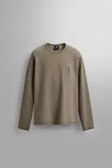 Camiseta relaxed fit de color verde militar, confeccionada en tejido con estructura waffle. Tiene cuello redondo, manga larga con puño elástico y un bolsillo plastrón con cierre de cremallera en el pecho.