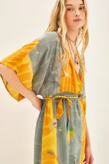 Vestido midi de estilo boho, confeccionado en viscosa con paneles alternados en colores amarillo y verde grisáceo. Presenta un estampado floral con detalles bordados en hilo de lurex, escote en V profundo, mangas anchas al codo y ajuste elástico en la cintura.