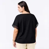 Remera negra de corte holgado y escote redondo, de manga corta con detalles de bordado y encaje macramé en las mangas.