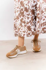 Zapatillas deportivas color blanco con detalles en beige y suela marrón.
