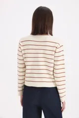 Cardigan de punto a rayas horizontales en color crema y marrón, con cuello redondo, cierre frontal de botones y dos bolsillos pequeños decorativos en la parte inferior.