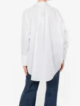 Camisa negra de corte oversize y manga larga con puños abotonados. Presenta un cuello clásico con un lazo fino para anudar en la parte superior y un diseño con bajo asimétrico, siendo más larga en la parte posterior.