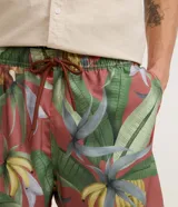 Bermuda de baño para hombre, color base rojizo/terracota, con estampado tropical de hojas verdes y bananas. Posee cintura elástica con cordón ajustable y bolsillos laterales.