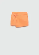 Falda corta de algodón estilo tejano, color naranja, con diseño cruzado y detalle de lazo ajustable con ojales metálicos en la cintura.