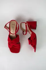Sandalia de tacón cuadrado medio, confeccionada en material textil tipo gamuza color negro. Presenta un diseño de tiras cruzadas con nudo en la parte delantera y una tira ajustable con hebilla metálica en el tobillo.